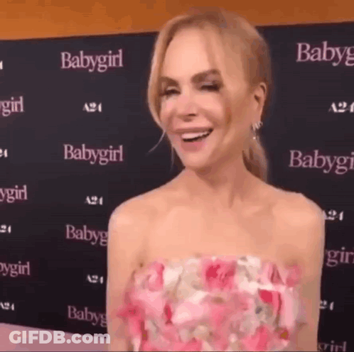 A Woman In A Pink Dress Is Smiling And Standing In Front Of A Wall With Babygirl Written On It . GIF