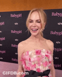 A Woman In A Pink Dress Is Smiling In Front Of A Wall With Babygirl Written On It GIF