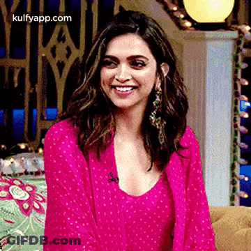 A Woman In A Pink Dress Is Smiling While Sitting On A Couch In A Room . GIF