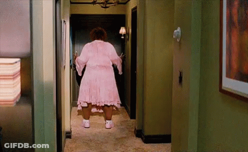 A Woman In A Pink Dress Is Standing In A Hallway . GIF