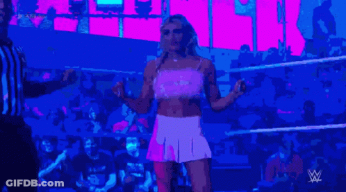 A Woman In A Pink Dress Is Standing In A Wrestling Ring With A Referee GIF
