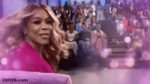 A Woman In A Pink Dress Is Standing In Front Of A Crowd . GIF