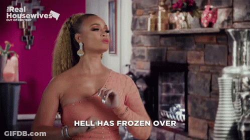 A Woman In A Pink Dress Is Standing In Front Of A Fireplace And Says " Hell Has Frozen Over " GIF