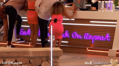 A Woman In A Pink Dress Is Standing In Front Of A Neon Sign That Says " Eat Drink On Repeat " GIF