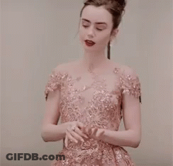 A Woman In A Pink Dress Is Standing In Front Of A White Wall . GIF