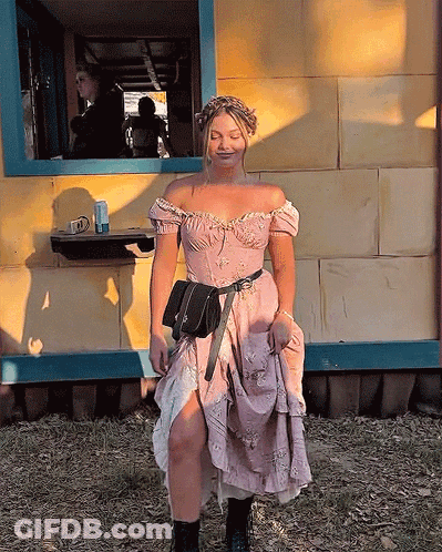 A Woman In A Pink Dress Is Standing In Front Of A Yellow Building GIF