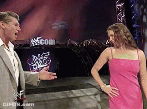 A Woman In A Pink Dress Is Standing Next To A Man In A Suit In Front Of A Sign That Says Wwe.com GIF