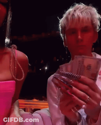 A Woman In A Pink Dress Is Standing Next To A Man In A White Shirt Holding A Stack Of 100 Dollar Bills GIF