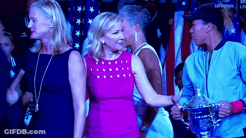 A Woman In A Pink Dress Is Standing Next To A Woman Holding A Trophy GIF