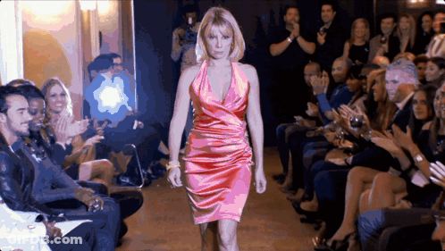 A Woman In A Pink Dress Is Walking Down The Runway GIF