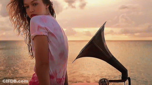 A Woman In A Pink Dress Stands In Front Of A Gramophone GIF