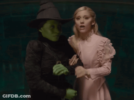 A Woman In A Pink Dress Stands Next To A Green Witch GIF