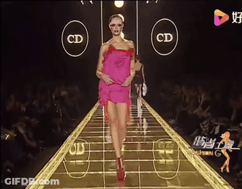 A Woman In A Pink Dress Walks Down A Runway With The Letters Cd On The Side GIF