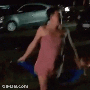 A Woman In A Pink Dress With A Bow On The Back Is Walking Down A Street At Night . GIF