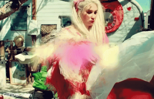 A Woman In A Pink Dress With Feathers Is Standing In Front Of A Trailer GIF
