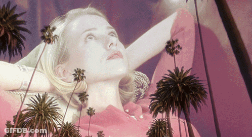 A Woman In A Pink Dress With Palm Trees Behind Her GIF