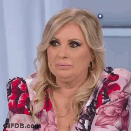 A Woman In A Pink Floral Dress Is Making A Funny Face While Sitting On A Chair . GIF