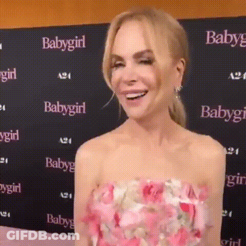 A Woman In A Pink Floral Dress Is Smiling In Front Of A Baby Girl Sign . GIF