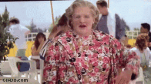 A Woman In A Pink Floral Dress Is Standing In Front Of A Crowd Of People . GIF