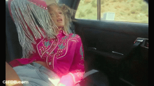 A Woman In A Pink Fringed Shirt Sits In The Back Seat Of A Car GIF