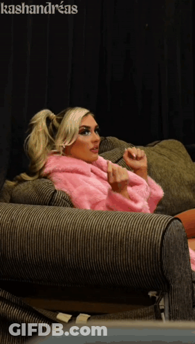 A Woman In A Pink Fur Coat Sits On A Couch With The Name Kashandreas On The Bottom GIF