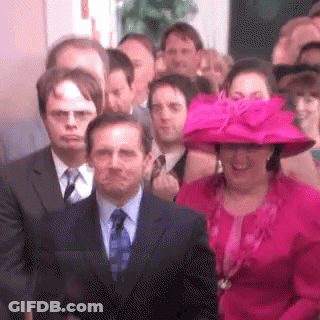A Woman In A Pink Hat Is Standing In Front Of A Crowd Of People In Suits And Ties . GIF