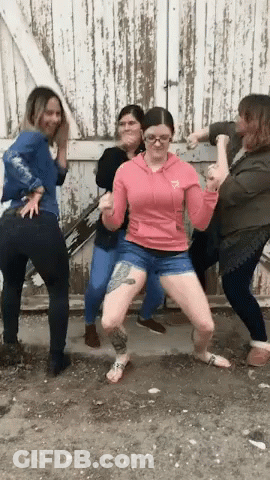 A Woman In A Pink Hoodie Has A Tattoo On Her Leg And Is Surrounded By Other Women GIF