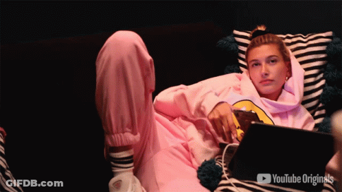 A Woman In A Pink Hoodie Is Laying On A Couch With A Youtube Originals Logo Behind Her GIF