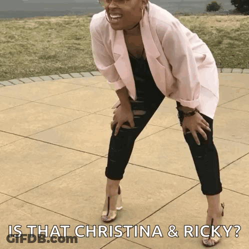 A Woman In A Pink Jacket And Black Pants Is Kneeling On A Sidewalk With The Caption Is That Christina & Ricky ? GIF