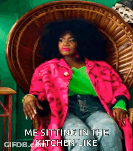A Woman In A Pink Jacket And Green Shirt Is Sitting In A Wicker Chair With The Caption Me Sitting In The Kitchen Like GIF