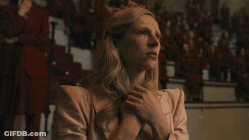 A Woman In A Pink Jacket Has Her Hands Folded In Front Of A Crowd GIF