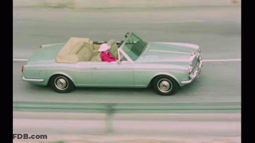 A Woman In A Pink Jacket Is Driving A Silver Convertible GIF