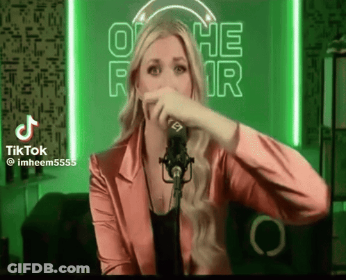 A Woman In A Pink Jacket Is Singing Into A Microphone In Front Of A Neon Sign That Says Othe Fair GIF