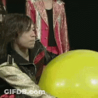 A Woman In A Pink Jacket Is Standing Next To A Yellow Balloon GIF
