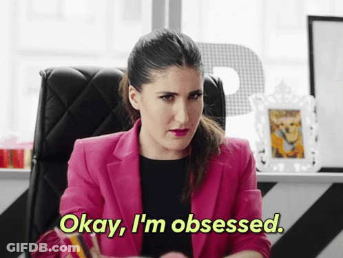 A Woman In A Pink Jacket Says " Okay I 'M Obsessed " While Sitting At A Desk GIF