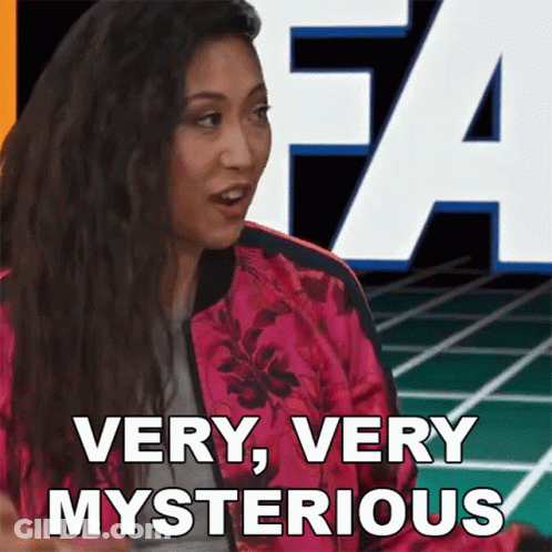 A Woman In A Pink Jacket Says Very Very Mysterious In Front Of A Large Letter A GIF
