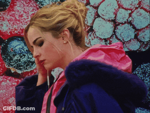 A Woman In A Pink Jacket With A Blue Fur Hood Looks Down GIF