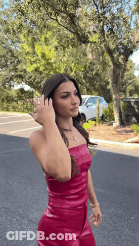 A Woman In A Pink Leather Dress Is Standing On The Side Of The Road . GIF