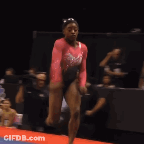 A Woman In A Pink Leotard Is Doing A Trick In Front Of A Sign That Says 215 GIF