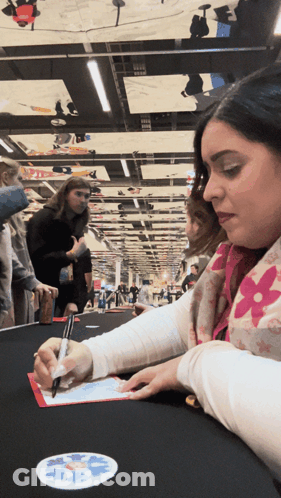 A Woman In A Pink Louis Vuitton Scarf Is Signing A Piece Of Paper GIF