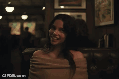 A Woman In A Pink Off The Shoulder Top Is Smiling In A Dark Room GIF
