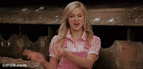 A Woman In A Pink Plaid Shirt Is Clapping Her Hands In A Barn GIF