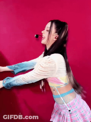 A Woman In A Pink Plaid Skirt Is Dancing In Front Of A Red Background GIF