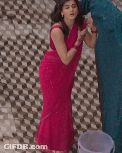 A Woman In A Pink Saree Is Standing Next To A Bucket On A Tiled Floor GIF