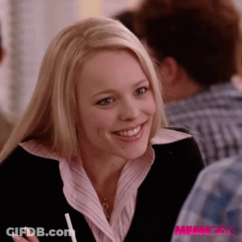 A Woman In A Pink Shirt And Black Jacket Is Smiling In Front Of A Sign That Says Meangirls GIF