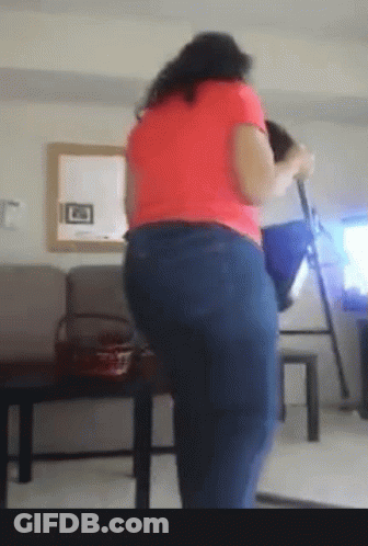 A Woman In A Pink Shirt And Blue Jeans Is Standing In Front Of A Mirror GIF