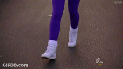 A Woman In A Pink Shirt And Purple Pants Is Jogging Down A Street . GIF