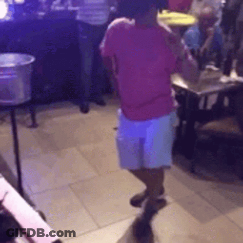 A Woman In A Pink Shirt And White Shorts Is Dancing In A Room With People . GIF