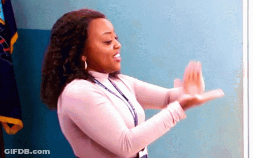 A Woman In A Pink Shirt Is Clapping Her Hands In Front Of A Flag . GIF
