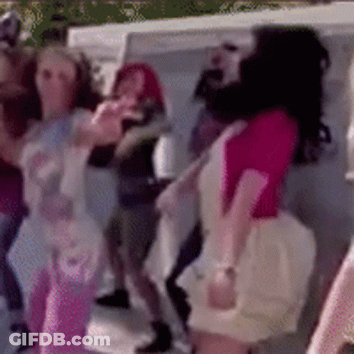 A Woman In A Pink Shirt Is Dancing In A Crowd Of People GIF